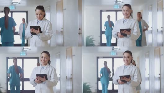 美丽的年轻女医生站在医院走廊，用平板电脑和迷人的微笑。工作中的专业人士。高清在线视频素材下载