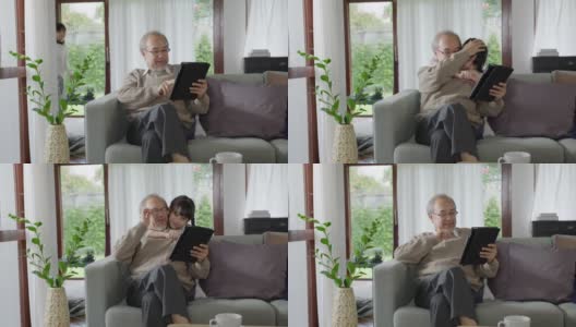 老的亚洲祖父母在家里用电脑平板电脑和孙子们一起玩和看，以增进家庭关系。年轻女孩从背后拥抱年长的男人。高清在线视频素材下载