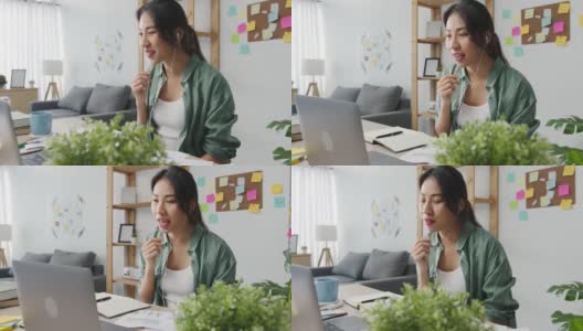 亚洲商业女性使用笔记本电脑与同事在视频通话中讨论计划，而智能工作在家客厅。高清在线视频素材下载