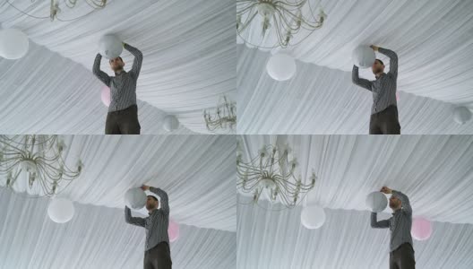 男人在天花板上挂着五颜六色的白粉灰纸灯笼。高清在线视频素材下载