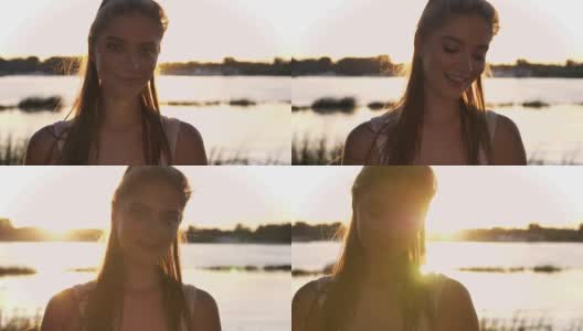 肖像的年轻迷人的女人看在相机和笑，日落和镜头光晕，河流和自然背景高清在线视频素材下载
