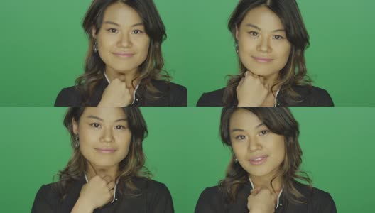 年轻的亚洲女人微笑着把她的头发放在她的头发后面，在一个绿色的屏幕工作室背景高清在线视频素材下载