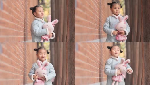快乐的中国女孩穿着蓝色的新年衣服，抱着她最喜欢的兔子玩具在户外跳舞，4-5岁，非常可爱，4k视频，慢镜头。高清在线视频素材下载
