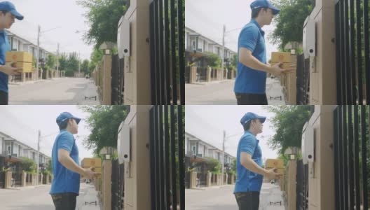 亚洲快递年轻男子身穿蓝色制服，微笑着拿着一堆纸箱在前屋村与复印空间。广告，商业，交通概念。高清在线视频素材下载