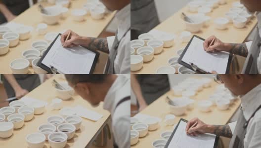 高角度的视角，专业的亚洲华人咖啡师评分者表演咖啡杯，品尝咖啡杯后在剪贴板上写下高清在线视频素材下载