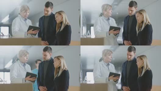 在医院的前台，医生拿着平板电脑与年轻夫妇交谈。高清在线视频素材下载