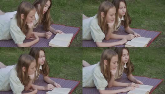 十几岁的女孩在暑假躺在绿色的草坪上看书。两个女朋友在夏日公园的草地上悠闲地看书。高清在线视频素材下载