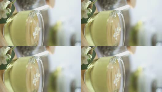 一滴茶落入一杯茉莉花绿茶。新鲜的茉莉花在杯子里和附近高清在线视频素材下载