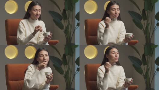 可爱的年轻女人坐在家里的椅子上吃酸奶高清在线视频素材下载