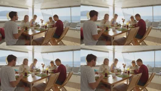 一群年轻漂亮的人在游艇上吃健康早餐，他们在友好地聊天。他们有各种各样的菜和冰沙上桌。海是背景。高清在线视频素材下载