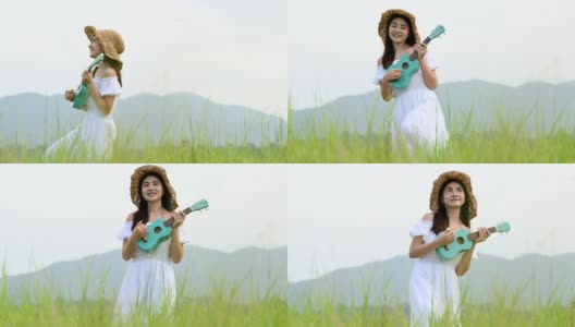 亚洲快乐的女人在白色的衣服弹奏尤克里里吉他在绿色的草地与山的背景在夏天。音乐家美女放松与乐器。乡村的生活方式高清在线视频素材下载