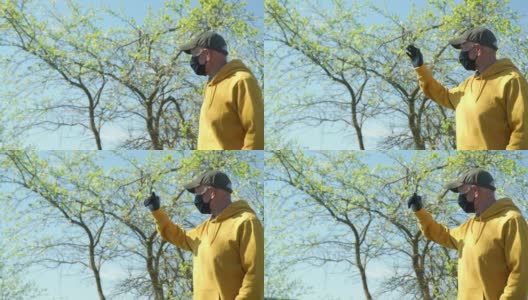 一位戴着黑色面罩和帽子的老人向绿树挥手高清在线视频素材下载