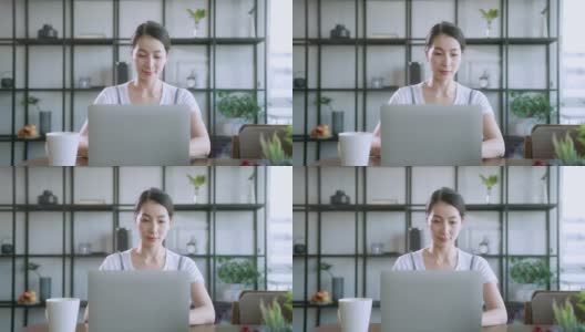 亚洲女性的妻子穿着休闲布在家工作，带着笔记本电脑，专注于餐桌的家庭背景，亚洲女性在家工作高清在线视频素材下载