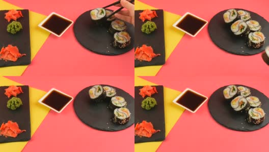 黑色的木条将阴阳寿司卷与鳗鱼和红色的鱼鲑鱼放在时尚的珊瑚黄色背景板上，绿色的山葵和粉红色的姜。极简主义风格的日本料理高清在线视频素材下载