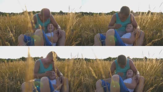 父亲在室外给小儿子挠痒痒。一个快乐的年轻人坐在草地上和他的宝贝儿子玩。快乐的爸爸和他的孩子一起在草地上玩。慢镜头高清在线视频素材下载