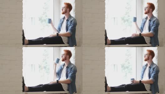 沉思的设计师喝咖啡，坐在窗前，红头发和红胡子高清在线视频素材下载