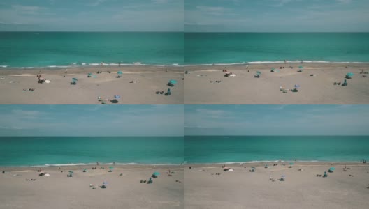 2021年3月春假和新冠肺炎期间，佛罗里达州朱诺海滩海滩海岸线上的彩色沙滩伞和人们的动态鸟瞰图高清在线视频素材下载