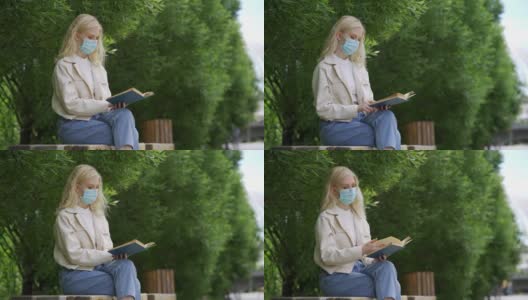 一名戴着医用口罩的学生在公园里看书。在冠状病毒流行期间进行户外学习。高清在线视频素材下载