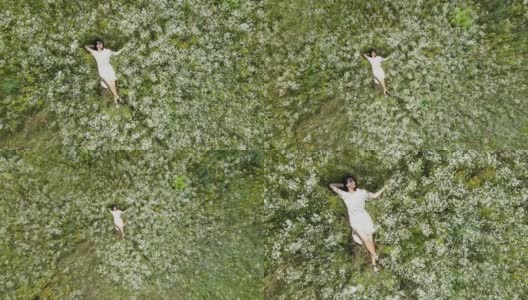 无人机鸟瞰图放松女人躺在鲜花盛开的草地，在农村，在夏天的一天，在田野里，感受自然，独自旅行。慢动作，俯视图。高清在线视频素材下载