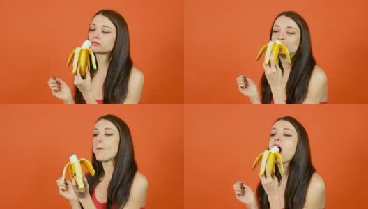 年轻健康的女人完美的皮肤吃香蕉明亮的橙色背景。热带水果。素食主义者的饮食概念高清在线视频素材下载