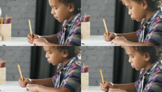 一个美国非洲男孩正坐在教室的桌子旁，在笔记本上做家庭作业高清在线视频素材下载