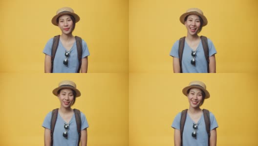 快乐青年亚洲妇女旅行者戴太阳镜帽子和背包微笑看着相机在空白的黄色背景。高清在线视频素材下载