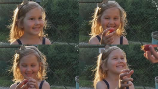 一个可爱的小女孩，带着美丽的微笑，从她妈妈的手中拿着成熟的草莓，高兴地吃着。特写,慢动作。高清在线视频素材下载