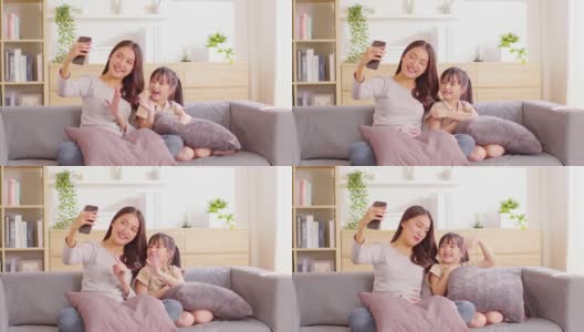年轻的亚洲妈妈和她的女儿视频电话会议与家人一起玩。幸福妈妈和小女孩一边看着手机一边挥着手和外婆视频聊天高清在线视频素材下载
