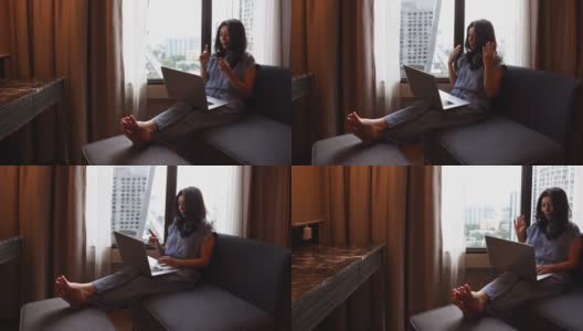 亚洲妇女视频电话笔记本电脑，而坐在现代椅子在酒店房间商务旅行。有魅力的女商人与家人进行远距离交流。高清在线视频素材下载