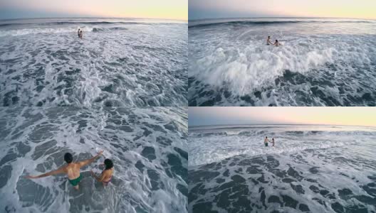 日落时分，一名年轻男子和一名少女在海里游泳，被海浪击中。汉普顿海滩，长岛，纽约州，美国。空中低空视频。高清在线视频素材下载