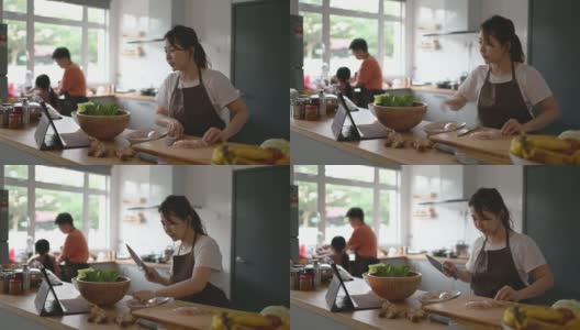 亚洲华人母亲在厨房柜台准备食物，并使用数字平板电脑通过互联网学习高清在线视频素材下载