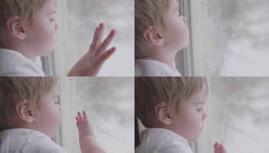 一个小孩站在窗边，看着雪花落在街上。拍在玻璃窗上的特写高清在线视频素材下载