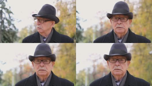 一位戴着眼镜和黑帽子的老爷爷在秋天的城市公园里散步高清在线视频素材下载