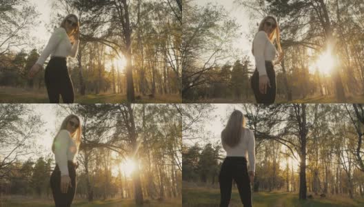 穿着毛衣、牛仔裤的迷人年轻女子在盛开的苹果树间翩翩起舞。日落，春天的果园和绿色的田野。慢动作高清在线视频素材下载
