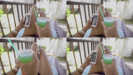 一个穿着泳衣的年轻女子正在度假，这位女士躺在帆布躺椅上，手里拿着一杯鸡尾酒和一部手机高清在线视频素材下载