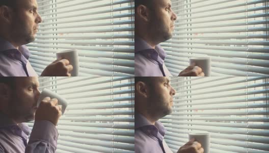 年轻的商人站在窗边喝咖啡。在办公室。一个严肃的人坐在窗外喝茶。深思熟虑的问题。老板喝咖啡，喝茶。疲倦、悲伤、沮丧的人会休息。高清在线视频素材下载