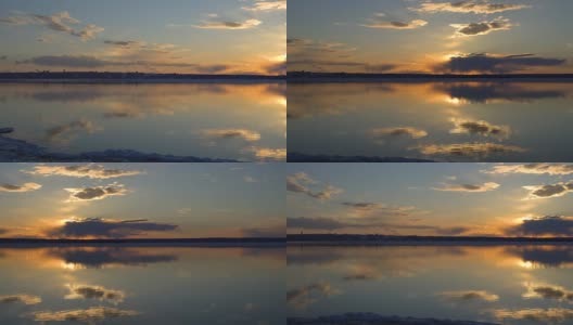 摄像机检查池塘(湖)的表面。水面部分被冰打开。没有风，因此湖面平静。云和天空倒映在水面上。在另一边可以看到城市。红日在日落高清在线视频素材下载