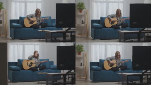 一个十几岁的女孩穿着家装，在温暖的客厅里坐在柔软的沙发上，弹奏着平静的旋律。她用手拉直了一绺金发。高清在线视频素材下载