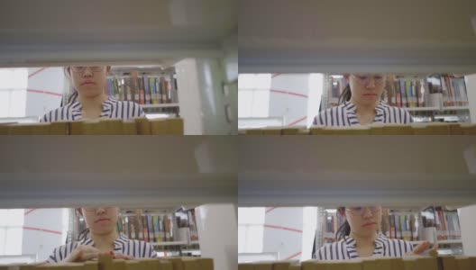 亚洲女孩在图书馆的书架上寻找书。高清在线视频素材下载