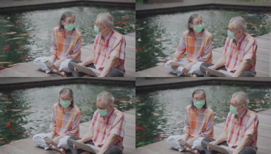 一对亚裔华人老年夫妇戴着外科口罩坐在地板上聊天高清在线视频素材下载