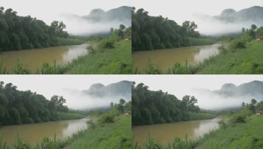 美丽的风景，一条河缓缓地流淌着，周围是郁郁葱葱的绿叶植物，雾气弥漫的山在早晨。山谷中的乡村景色。高清在线视频素材下载