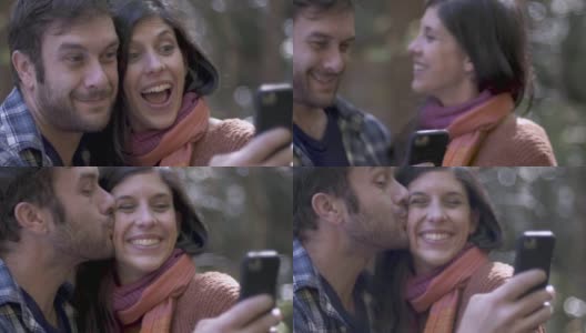 一名男子一边用智能手机自拍一边亲吻一名女子的脸颊高清在线视频素材下载