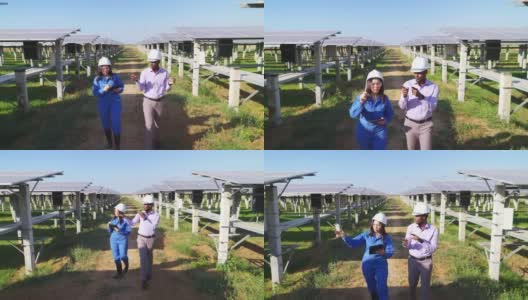 非洲投资者和亚洲中年女工程师身穿蓝色防护服，戴着安全眼镜、头盔在太阳能农场边走边谈，正面高角度观看高清在线视频素材下载