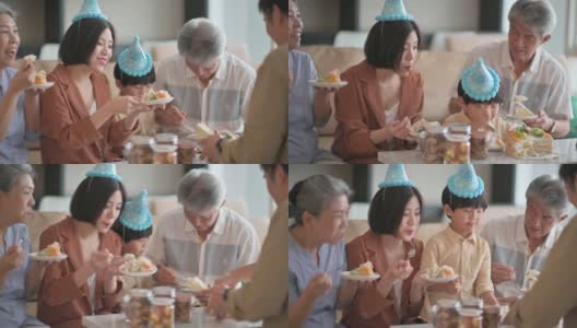 亚洲华人多代同堂庆祝生日，孙子戴着派对帽在客厅吃生日蛋糕高清在线视频素材下载