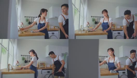 亚洲漂亮的年轻夫妇穿着围裙，在家里打扫厨房。新婚漂亮的人们男女感到幸福，享受在家里的房间里擦拭和搓揉。活动关系的概念高清在线视频素材下载