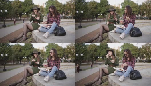 在公园里野餐。两个时髦女孩一边聊天一边吃三明治。这个节日三明治。高清在线视频素材下载