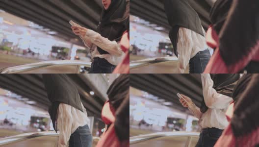 两名穆斯林妇女戴着头巾站在路边，用手机呼叫出租车取车服务，城市夜间公共交通移动应用方便便捷的城市城市智能生活高清在线视频素材下载