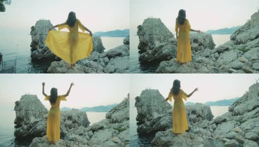 夏日的傍晚，年轻的黑发女郎站在海边的岩石上移动着身体高清在线视频素材下载