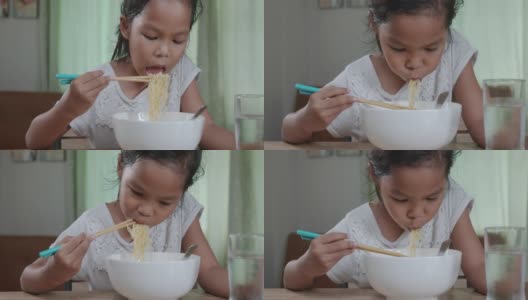 可爱的亚洲小女孩在家里用筷子吃美味的方便面。慢动作镜头。高清在线视频素材下载