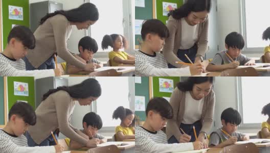 亚洲学校的老师在课堂上帮助学生。年轻女子在学校工作，帮助男孩写作，教育，支持和关心高清在线视频素材下载